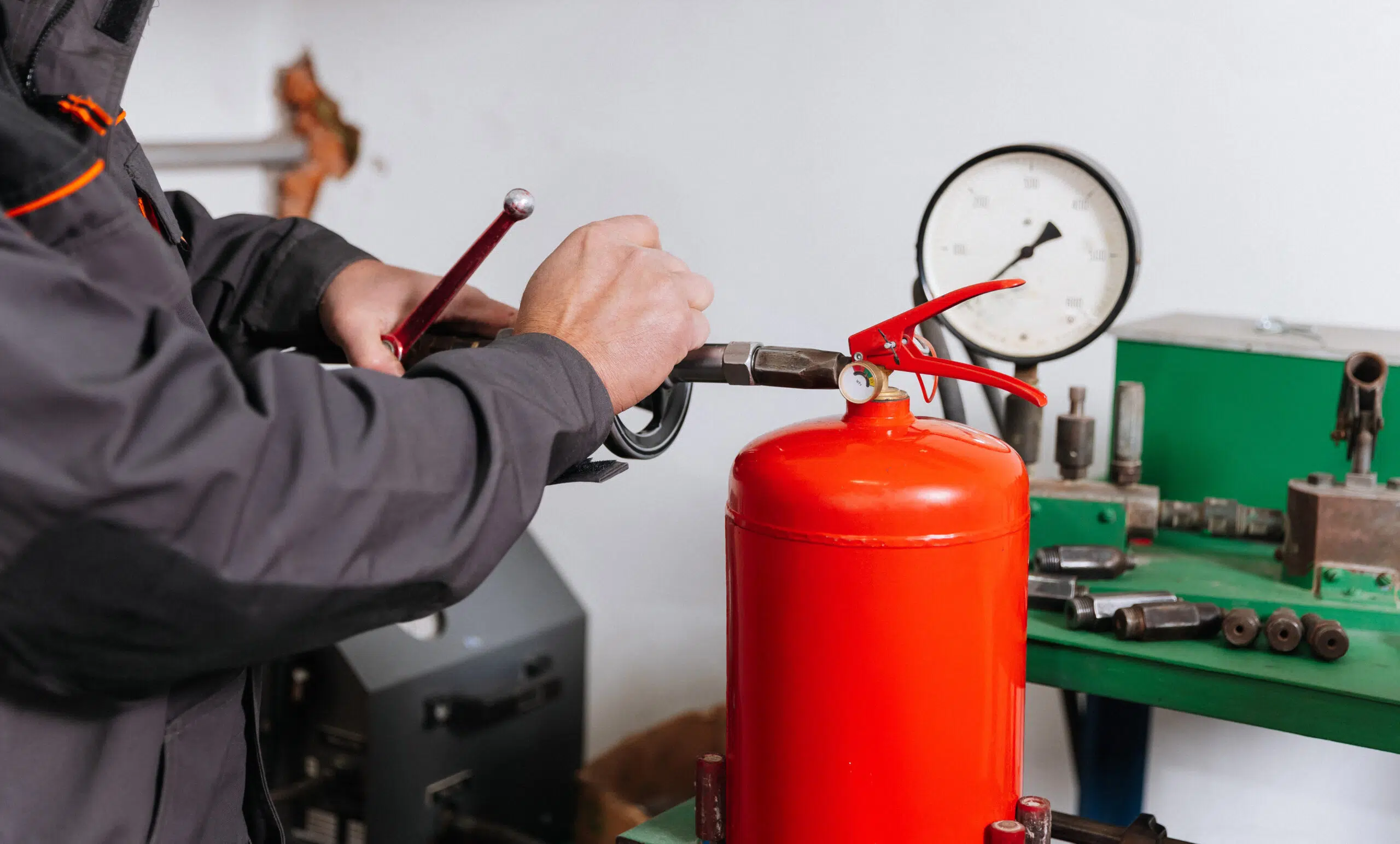 Technician refilling red fire extinguisher during pressure testing at workshop.